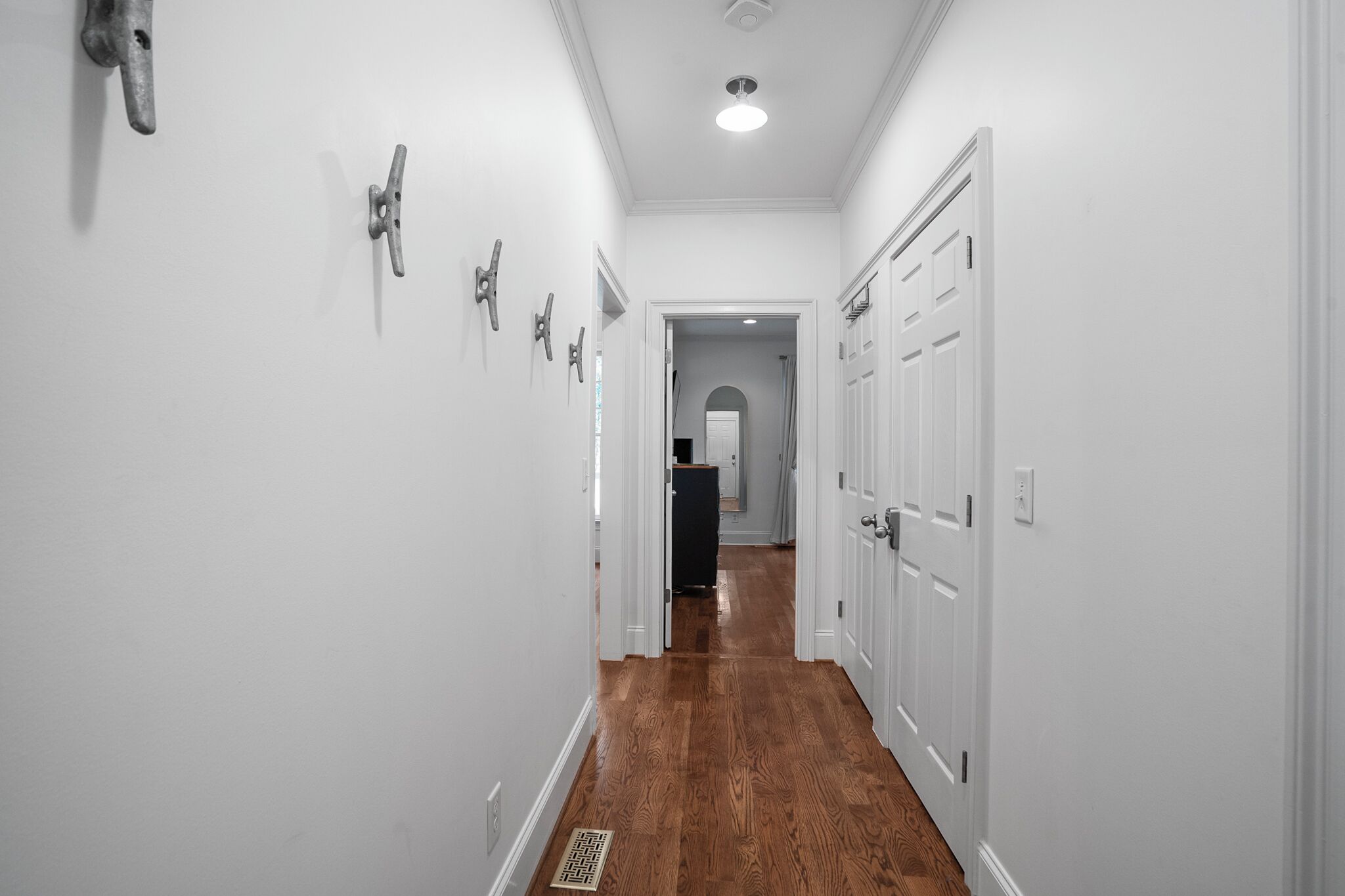Un couloir étroit aux murs blancs, au plancher en bois et aux portes blanches.