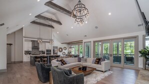 A spacious living area with a large sectional sofa, a coffee table, and a fireplace. There is a kitchen in the background with modern appliances and a dining area. - Private Pool+Game Room+Private Dock on Lake Oconee (Eatonton)
