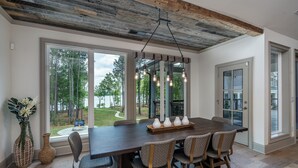A dining area with a large wooden table, six chairs, and a hanging light fixture. - Private Pool+Game Room+Private Dock on Lake Oconee (Eatonton)