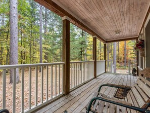 A covered porch with wooden railings and benches, overlooking a forested area. - Peaceful Pine Retreat in the Heart of Nisswa (Nisswa)