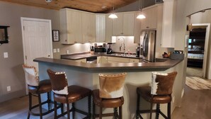 Een keuken met een centraal eiland, barkrukken, roestvrijstalen apparatuur en lichtkleurige keukenkastjes.