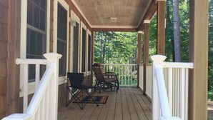Een houten veranda met een witte balustrade, twee zwarte stoelen en een tafel.