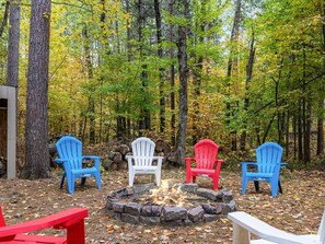 Escena de bosque con un hoyo para fuego y sillas Adirondack.