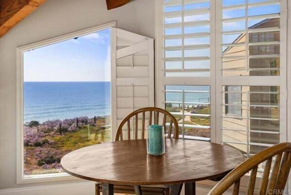 Enjoy ocean views and garden scenery from this room's large window, featuring a round table and a single chair.