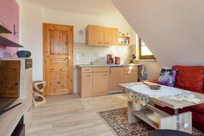 A compact kitchen with wooden cabinets, a dining table with a floral tablecloth, and a red sofa.