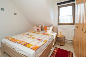 A bedroom with a bed, pillows, a nightstand, a window, and a radiator.