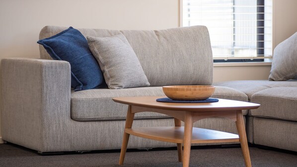 A modern living room with a grey sofa, a blue pillow, and a wooden side table with a bowl.