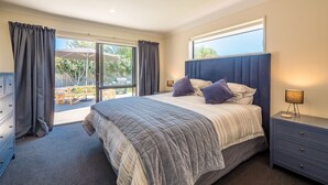 A bedroom with a large bed, a nightstand, a dresser, and a view of the outdoors. - A spacious family home in the centre of Mapua, close to everything but at the end of a quiet road (Mapua)