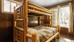 A bunk bed with a quilt, wooden walls, and a window with curtains.