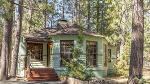 A small, single-story cabin with a porch, surrounded by trees.