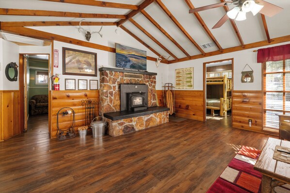 L’intérieur d’un chalet rustique, avec une cheminée en pierre, des poutres en bois, une table à manger et une vue sur l’extérieur.