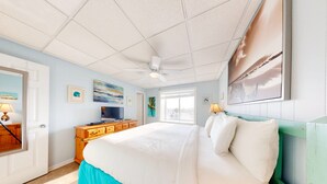 A bedroom with a bed, a ceiling fan, a TV, and artwork on the walls.