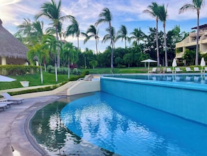 Una piscina con sillones de descanso y una estructura con techo de paja.