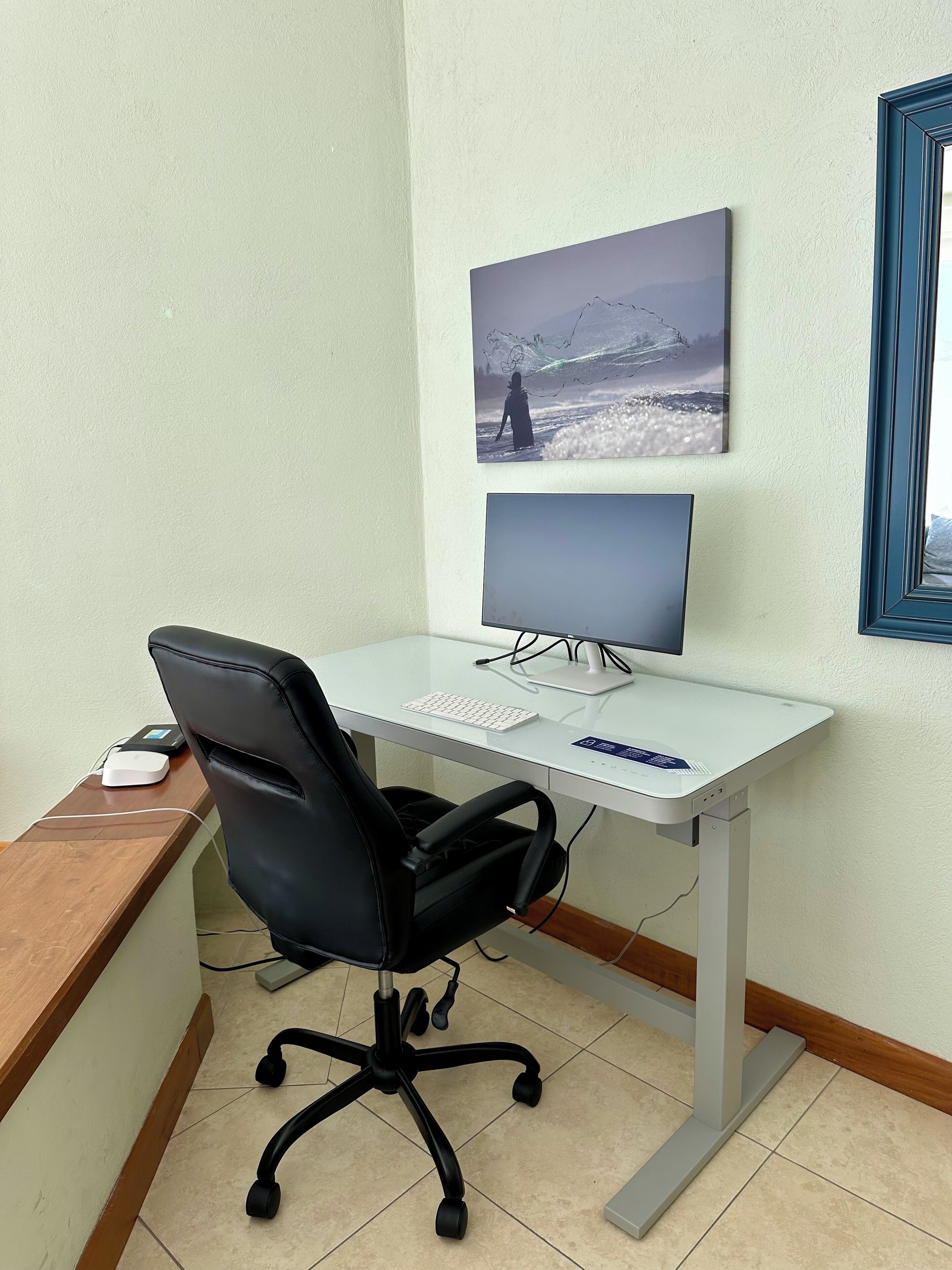 Ein kleiner Büroraum mit Schreibtisch, Stuhl, Computer und einem gerahmten Bild an der Wand.