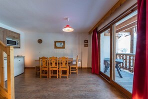 Een eethoek met houten stoelen en een tafel, een magnetron, een klok en een plafondlamp.