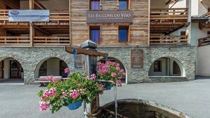 A building with a stone facade, wooden balconies, and hanging flower baskets. - Escapade alpine | Piscine, sauna & vue montagne (Abriès)
