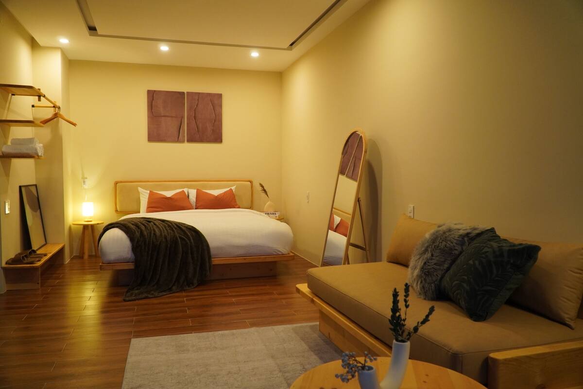 A bedroom with a bed, bedside table, lamp, mirror, and a sofa.