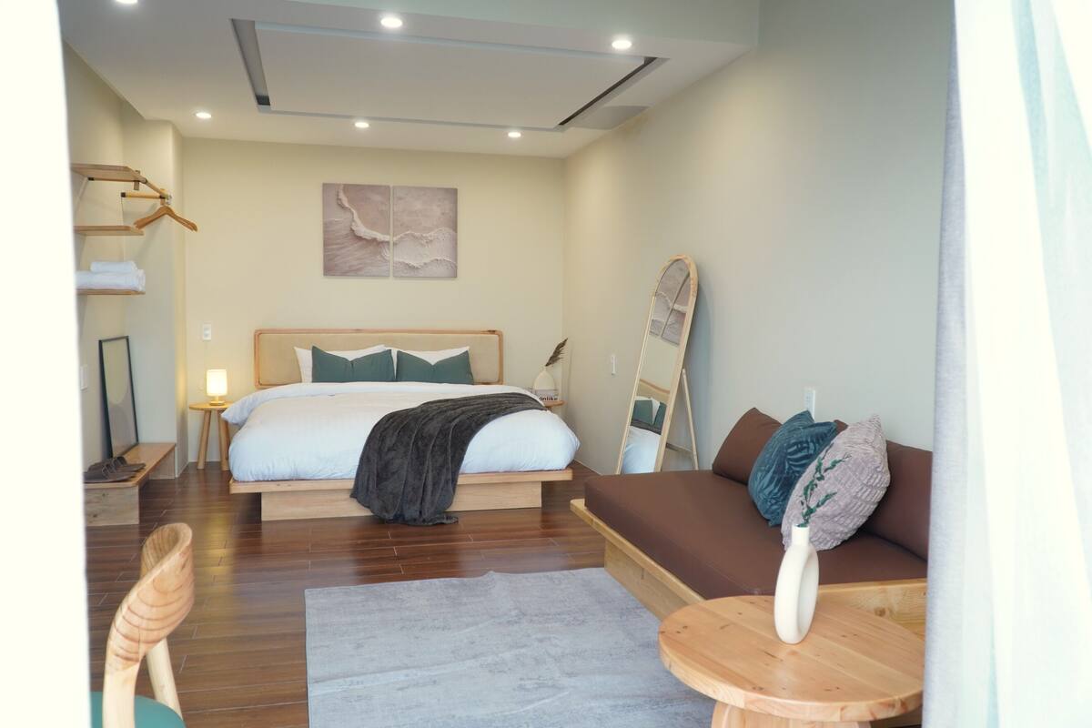 A modern hotel room with a large bed, a sofa, a wooden table, and a mirror.