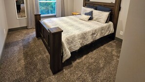 Une chambre à coucher avec un lit, un ventilateur de plafond, une fenêtre avec des rideaux et un sol recouvert de moquette.