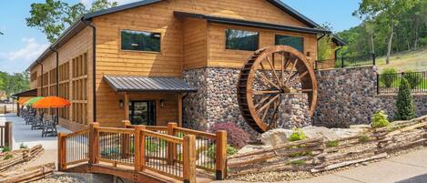 A wooden building with a large water wheel, a stone wall, and a wooden bridge.