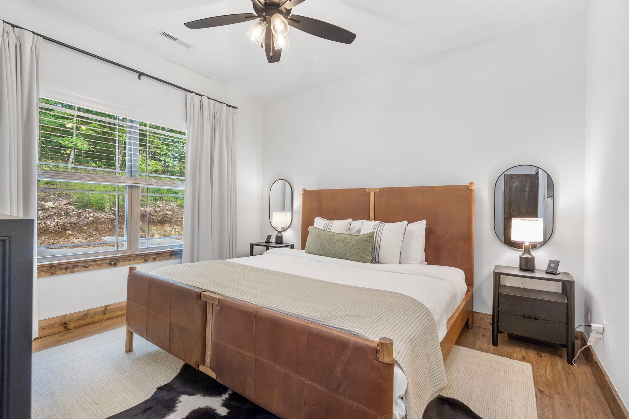 A bedroom with a bed, two bedside tables, a ceiling fan, and a window with curtains.