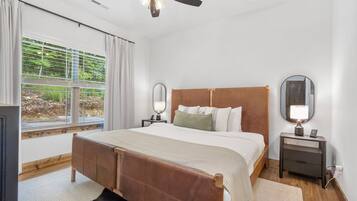 A bedroom with a bed, two bedside tables, a ceiling fan, and a window with curtains.