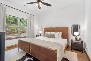 Un dormitorio con una cama, dos mesitas de noche, un ventilador de techo y una ventana con cortinas.