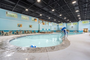 Una piscina interior con borde de azulejos, rodeada de sillas de descanso y una zona junto a la piscina.