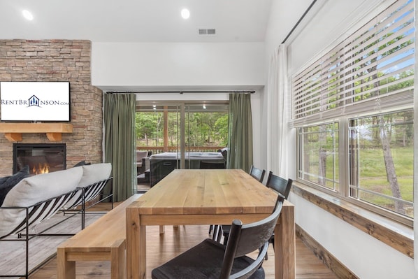 A spacious room with a large wooden dining table, comfortable seating, a fireplace, and a view of the outdoors.