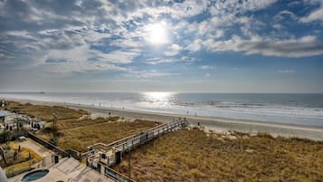 Vista de la playa con un paseo marítimo de madera que conduce a una zona de piscina.