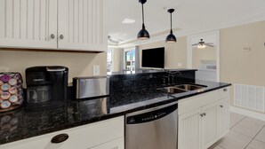 Une cuisine moderne avec des meubles blancs, un plan de travail en granit noir, une machine à café, un grille-pain et un lave-vaisselle.