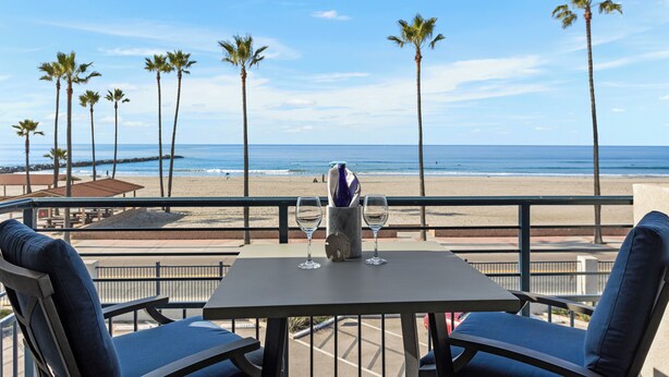 A balcony with a table and two chairs, overlooking a beach with palm trees and the ocean. - Beach Retreat, Free Wifi 308A (Oceanside)