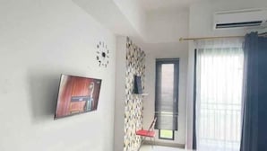 A room with a TV mounted on the wall, a window with blinds, and a patterned wall.