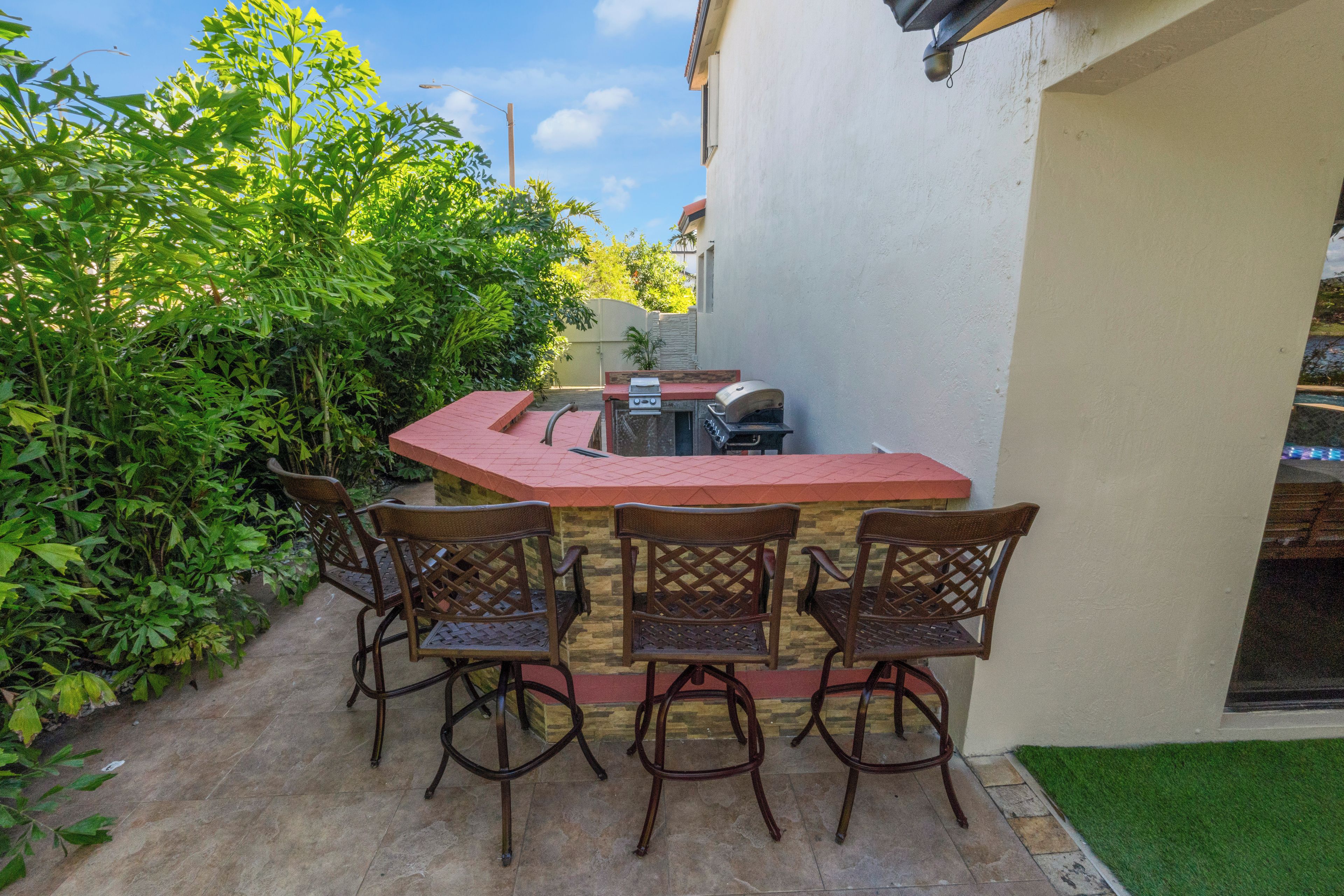 An outdoor patio with a red table and four wicker chairs, a barbecue grill, and a small gas stove.