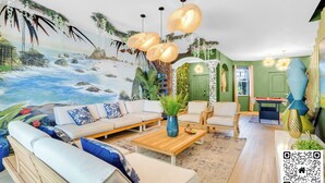 Sala de estar com um mural de uma cena de praia, um conjunto de sofás, uma mesa de centro e luminárias pendentes.