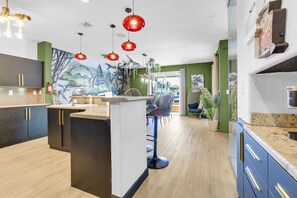 A modern kitchen with a central island, bar stools, and a mural on the wall. - Themed Glow Villa • 4K Cinema • Heated Pool • Lake • Sleeps 12 (Miami)