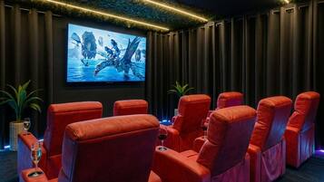 A cinema room with red reclining seats, a large screen, and a ceiling with a leaf pattern.
