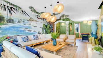 Sala de estar con un mural de playa, un conjunto de sofá, una mesa de centro y una zona de comedor con una mesa y sillas.