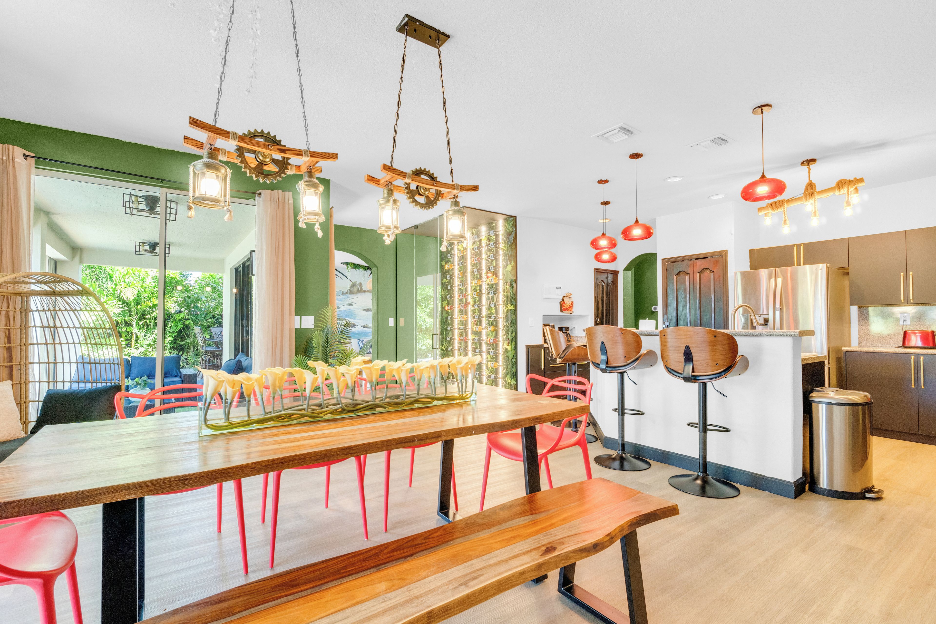 Cocina moderna con electrodomésticos de acero inoxidable, una mesa de comedor de madera con sillas rojas y vistas a la vegetación exterior.