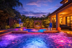 A heated outdoor pool with two basketball hoops, surrounded by lush greenery and a brick wall. - Themed Glow Villa • 4K Cinema • Heated Pool • Lake • Sleeps 12 (Miami)