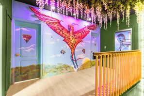 A hallway with a mural of a winged creature, a staircase, and a door with a triangular window. - Themed Glow Villa • 4K Cinema • Heated Pool • Lake • Sleeps 12 (Miami)