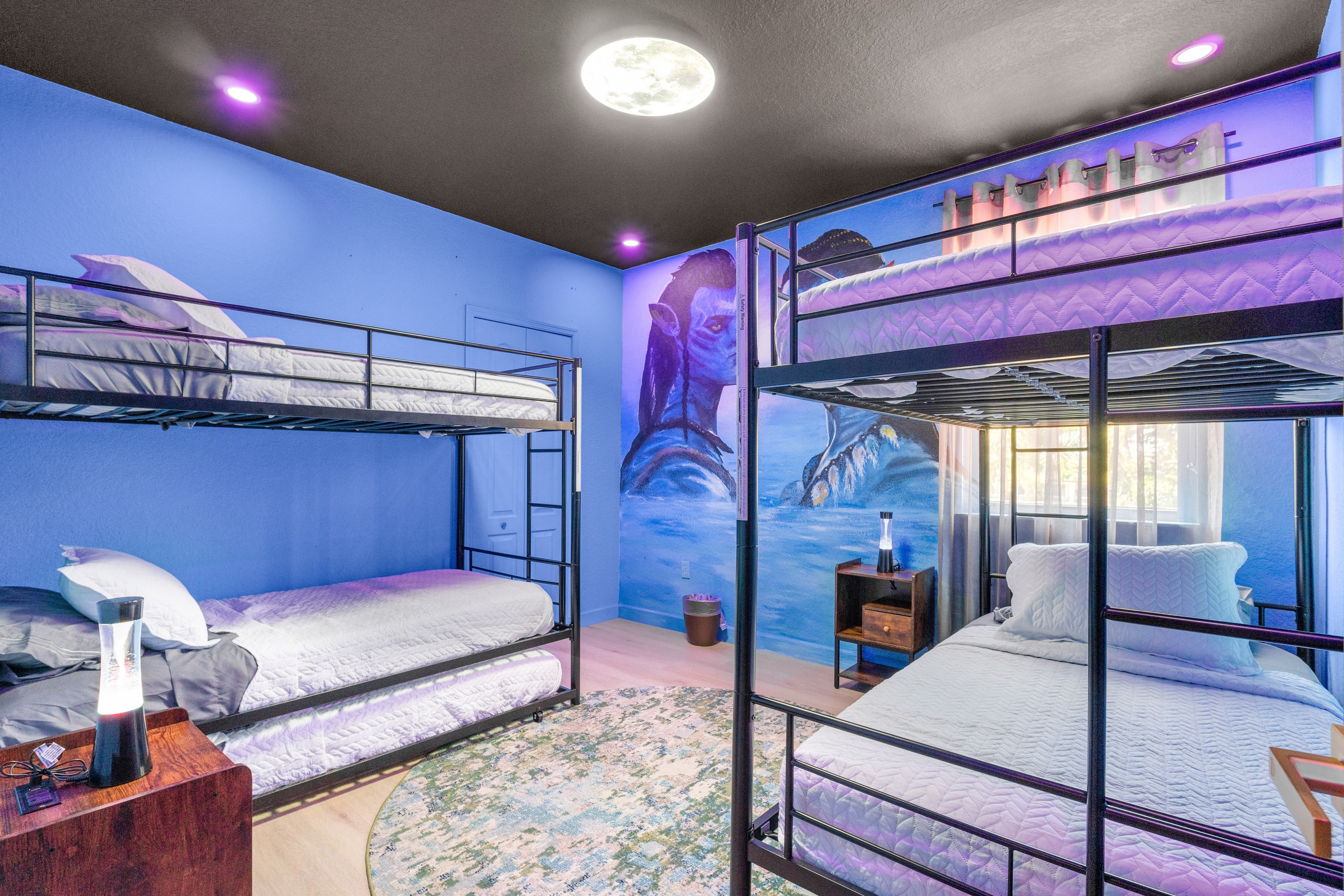 A bunk bed room with a mural on the wall, a round rug, and a nightstand with a lamp.