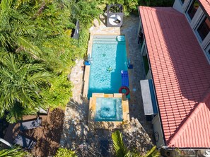 An aerial view of a swimming pool with a tiled deck, surrounded by lush greenery and a red-roofed building. - Themed Glow Villa • 4K Cinema • Heated Pool • Lake • Sleeps 12 (Miami)