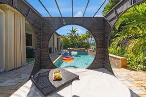 A pool area with a circular viewing frame, a lounge chair, and a fruit tray. - Themed Glow Villa • 4K Cinema • Heated Pool • Lake • Sleeps 12 (Miami)