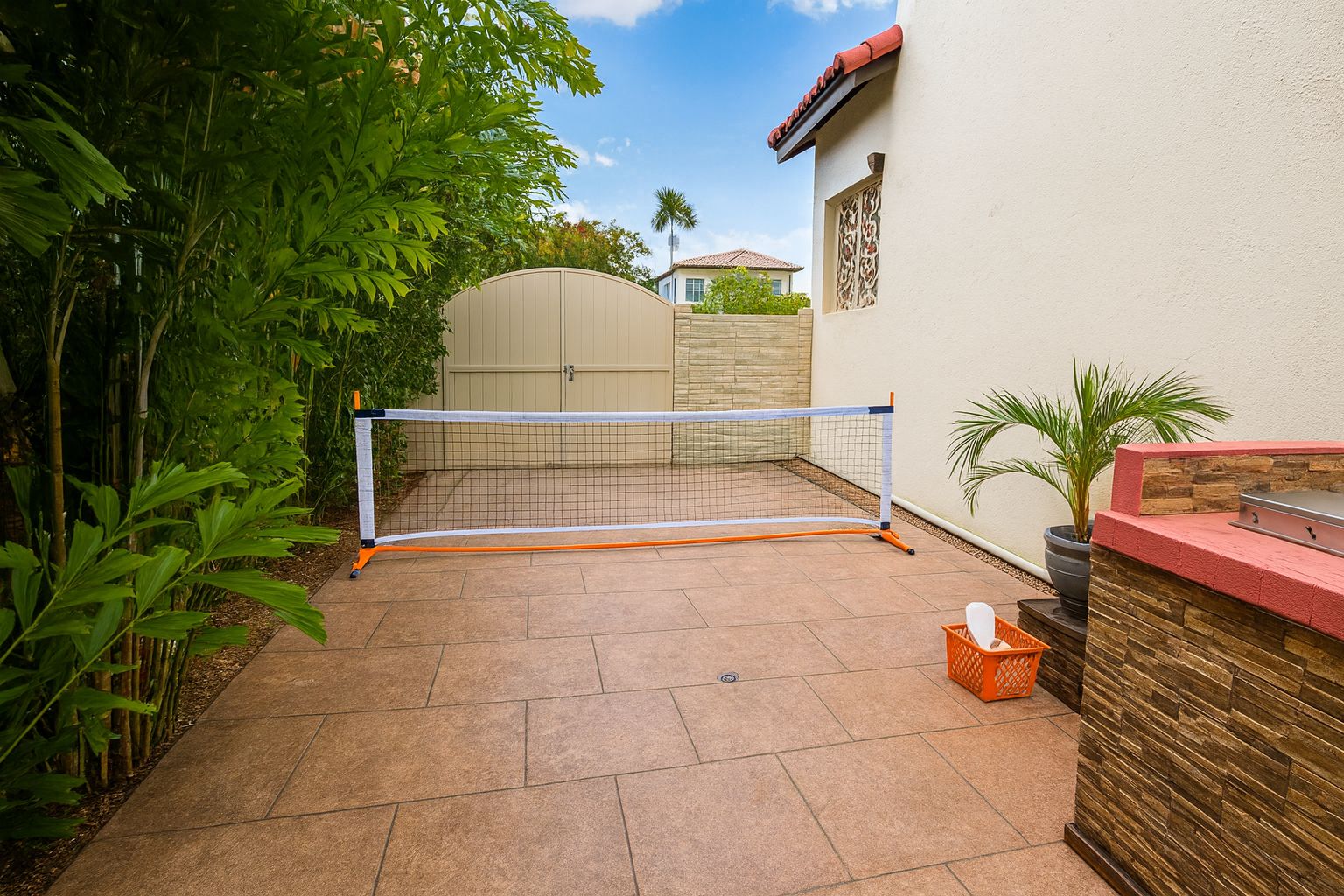 A backyard with a tennis net, a patio area, and a stone wall with a grill.