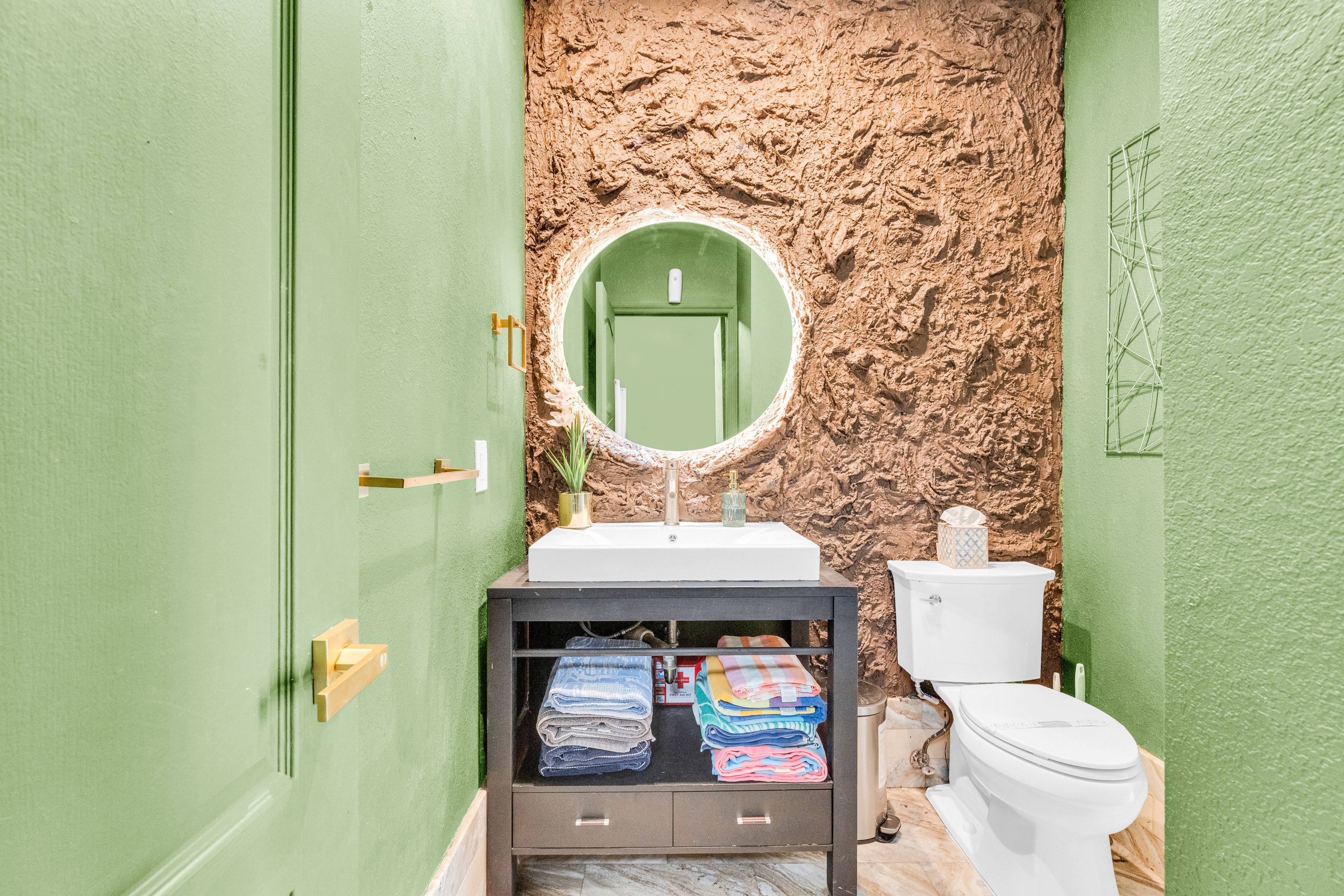 Een badkamer met een groene deur, een wastafel met spiegel, een toilet en een plank met handdoeken.