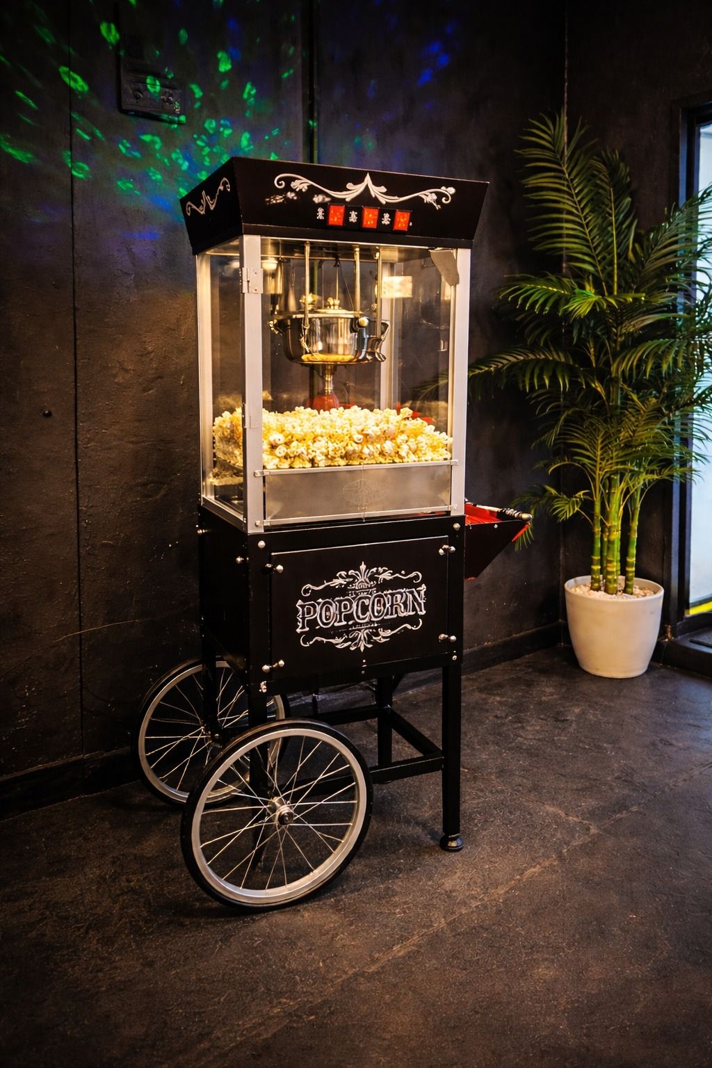 A popcorn vending machine with a glass enclosure, wheels, and a decorative top.