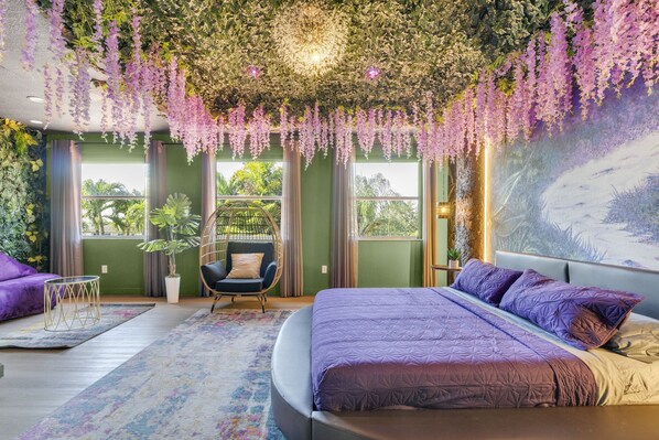 A bedroom with a large bed, a hanging chair, and a view of greenery outside. - Themed Glow Villa • 4K Cinema • Heated Pool • Lake • Sleeps 12 (Miami)