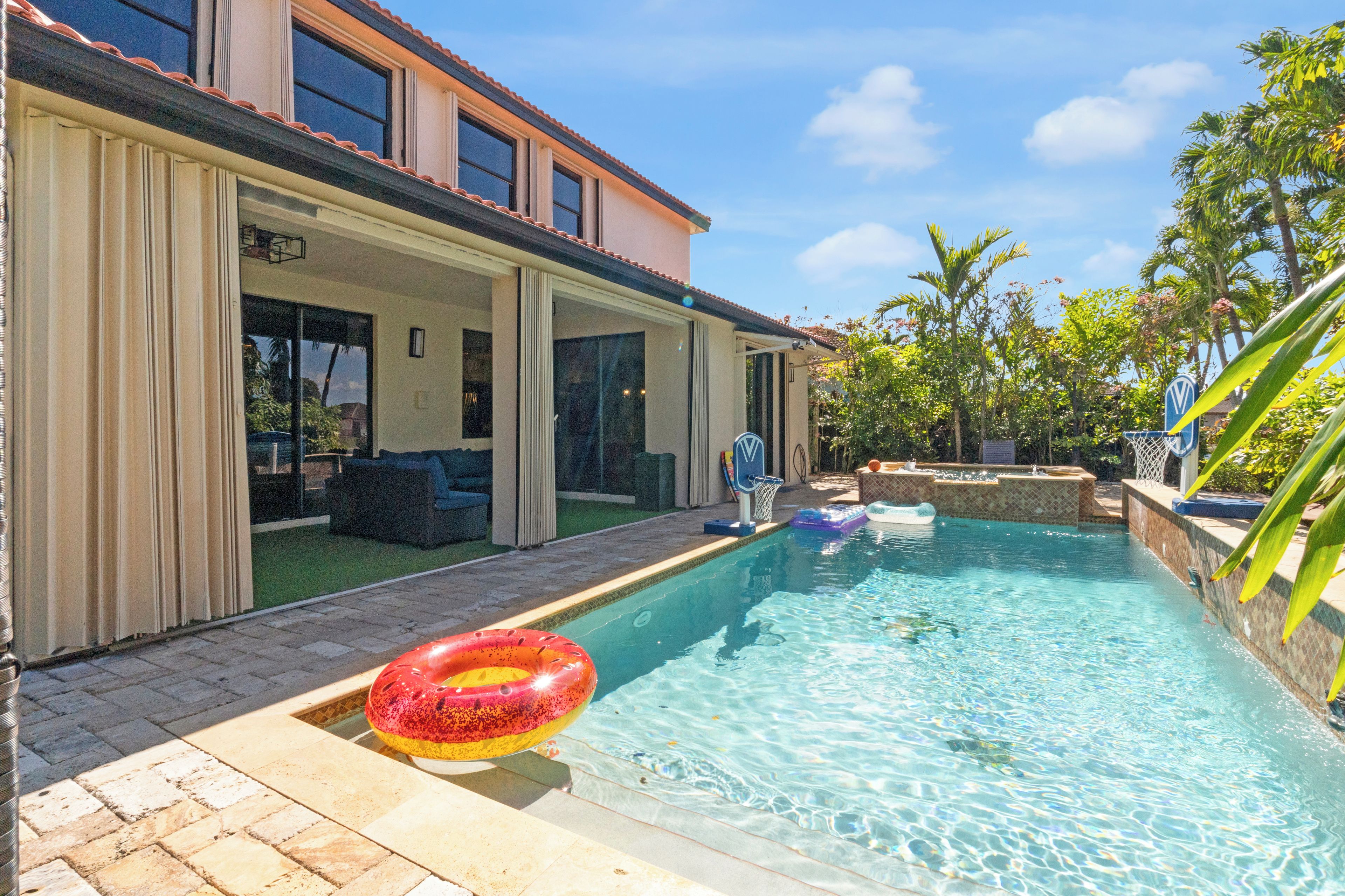A swimming pool with a hot tub, a lounge area with a sofa, and a view of a house with a balcony.