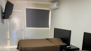 A hotel room with two beds, a flat-screen TV mounted on the wall, an air conditioning unit, and a window with a lighted frame. - Double Suite- 500m from "La Lomita". (Culiacán Rosales)